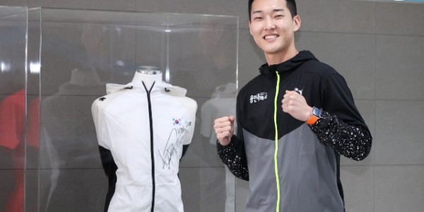 우상혁 선수가 자신이 지난 대회 때 착용했던 유니폼 전시대 앞 기념 촬영을 하고 있다..JPG